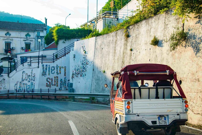 A vintage car parked by a wall with graffiti and a building with a sign reading 'Costa del Marmi.' 5