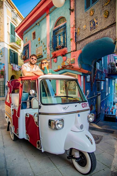 A vintage white vehicle with 'CITY' on the front, parked on a street with colorful buildings. 2