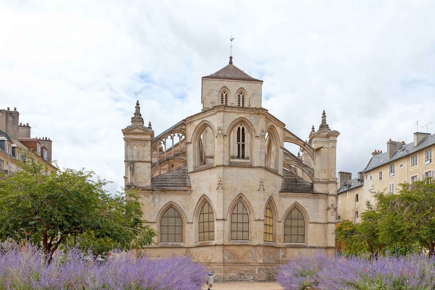 A historic church with a bell tower, arched windows, and a surrounding garden with purple flowers. 5