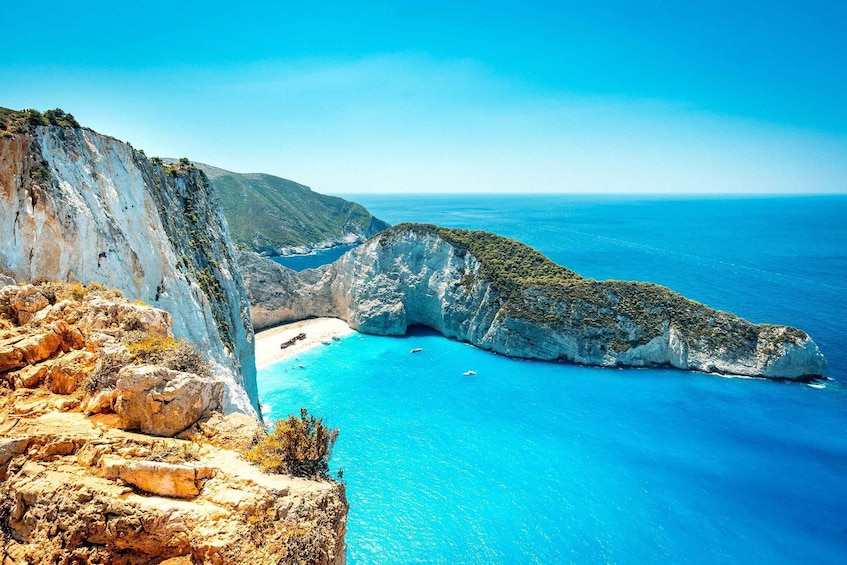 A coastal landscape with a prominent cliff, a cove, and clear blue waters. 4