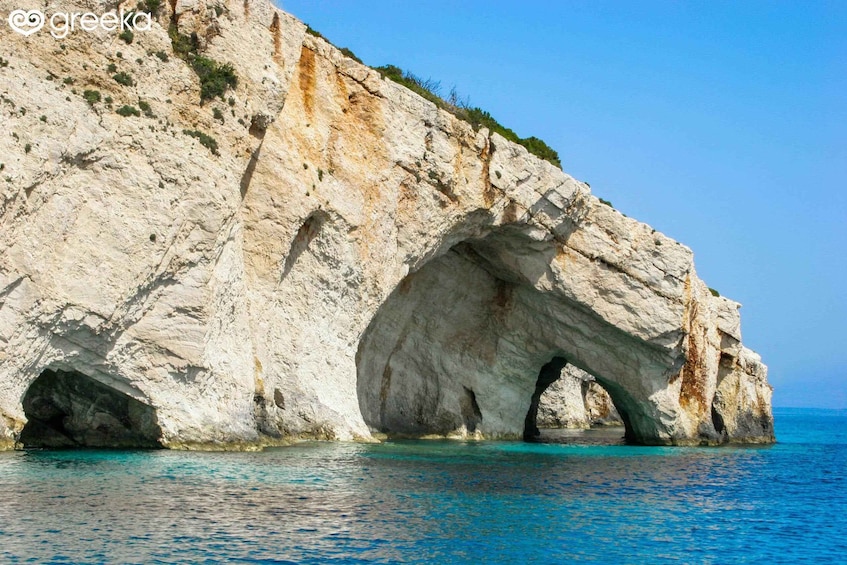 A white rock formation with a natural arch over turquoise water. 3