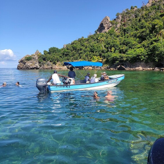 A clear blue boat with people swimming in the water, surrounded by lush greenery and rocky cliffs. 5