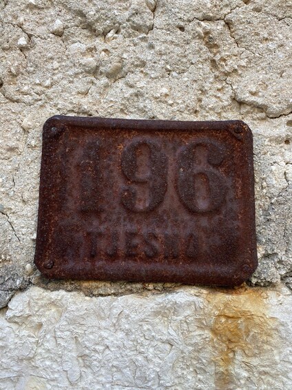 A weathered metal plaque with the inscription '196' and 'FLESIA' on a textured stone wall. 3