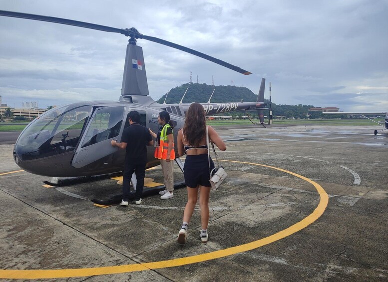 A helicopter on a tarmac with people boarding, a clear sky, and a distant hill. 1