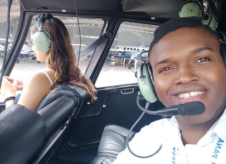 A person in a vehicle wearing a headset, with another person in the background. 2