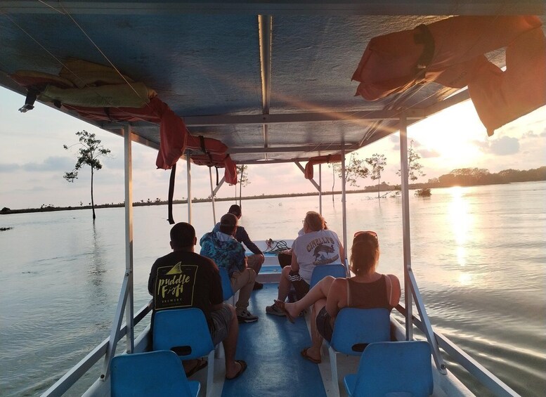A group of people on a boat with a covered canopy, looking out over calm water at sunset. 4