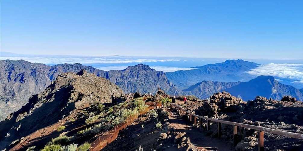 A mountainous landscape with a clear sky, rocky terrain, and a trail with a wooden fence. 4