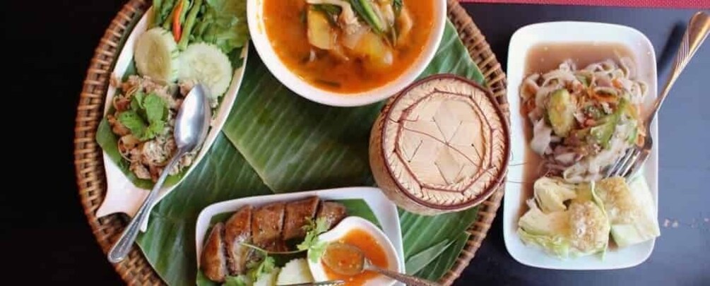 A variety of dishes served on a banana leaf tray, including a bowl of soup, a plate of meat, and a dish with noodles and vegetables. 2
