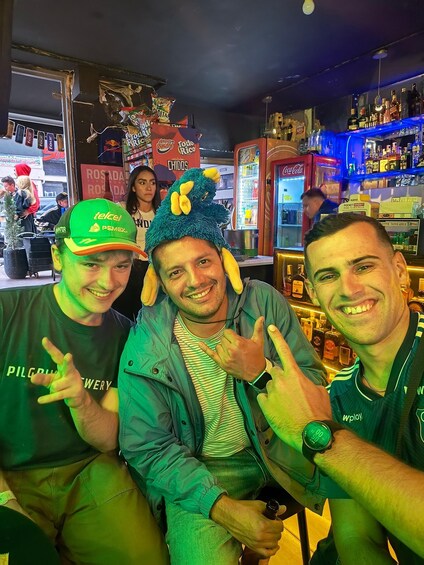 Three people in a bar with a neon sign, a Coca-Cola machine, and various bottles. 2