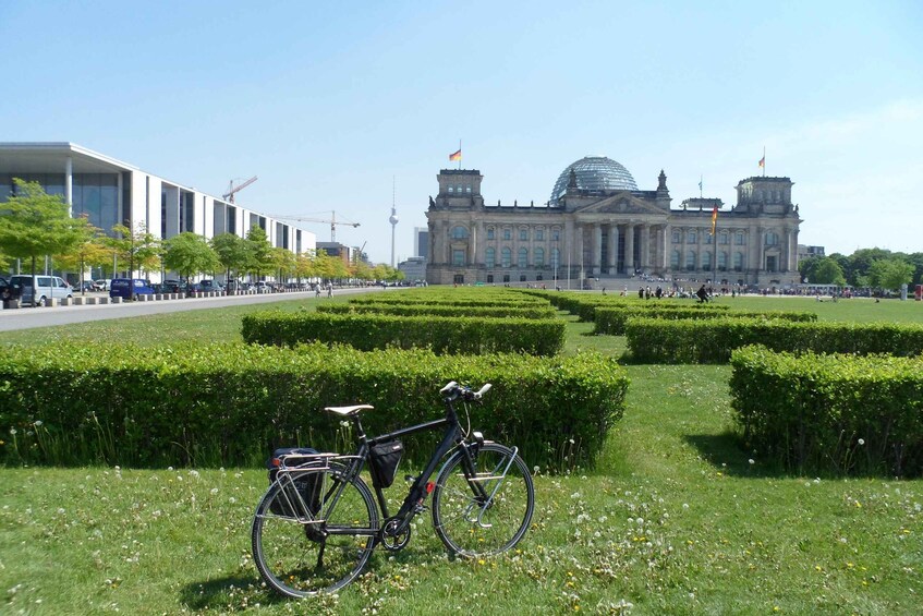 A bicycle parked on grass with a large building and a dome in the background. 5