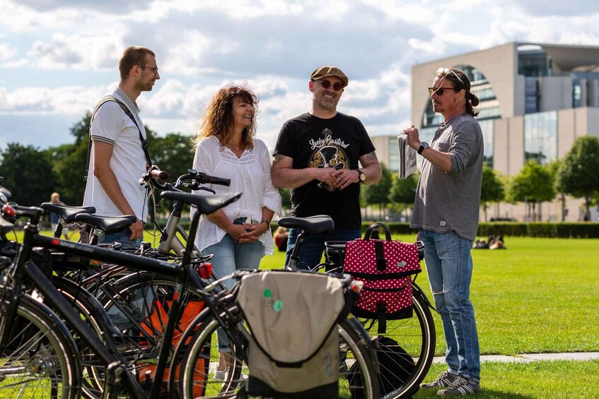 A group of people standing outdoors with bicycles and a modern building in the background. 4