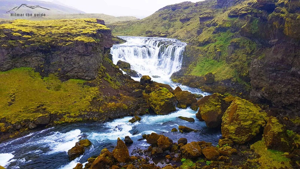 A waterfall cascading over rocks in a green valley. 5