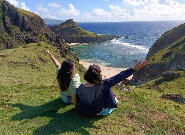 Two people sitting on a grassy hill overlooking a coastal landscape with cliffs and the ocean. 3