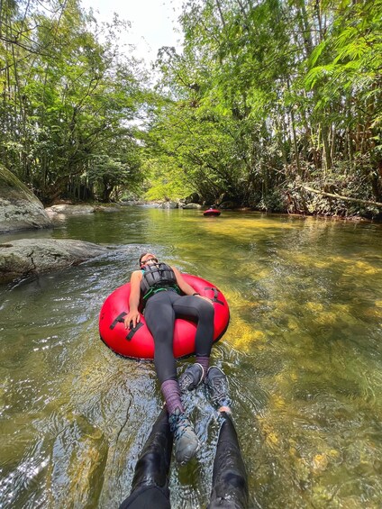 A person floating on a red tube in a river surrounded by dense green foliage. 2