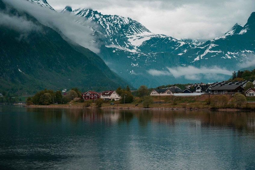 A tranquil lake with houses on the shore, surrounded by snow-capped mountains and dense forest. 5