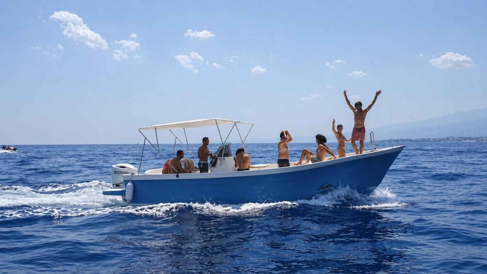 A blue boat with people on board, some standing and some sitting, on a calm sea with a clear sky. 2