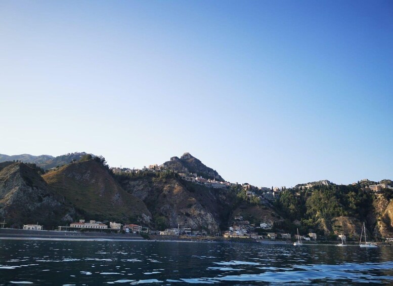 A coastal town with buildings on hills, a clear sky, and calm sea. 4