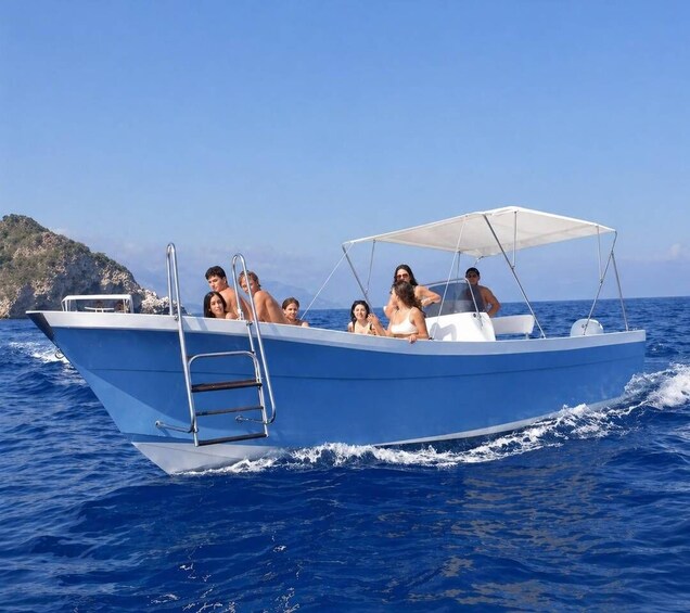 A blue boat with a white canopy, passengers, and a rocky coastline in the background. 1