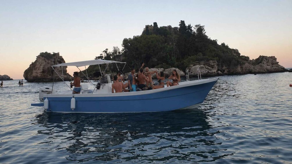 A blue boat with people on it, moving on calm water with a rocky island in the background. 3