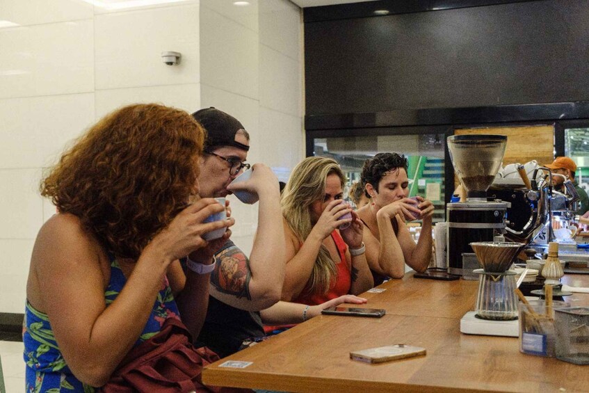 A group of people sitting at a table in a cafe, with coffee machines and a window in the background. 1