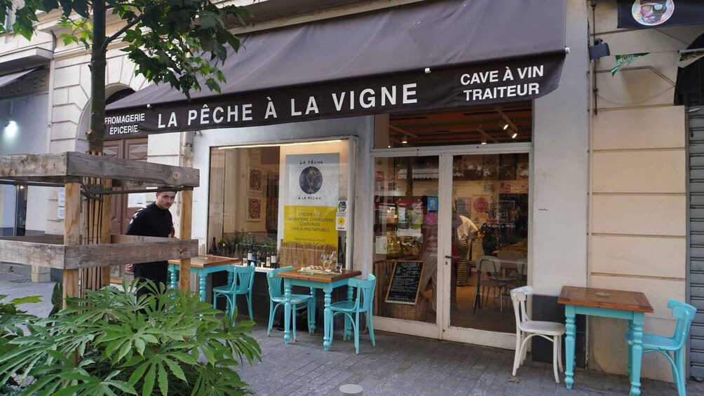 A café named 'La Pêche à la Vigne' with outdoor seating and a signboard advertising 'Cave à Vin Traiteur'. 4