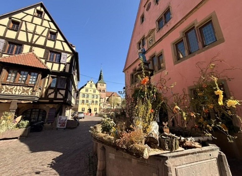 A cobblestone street with traditional half-timbered houses, a church steeple, and a flower-adorned planter. 5