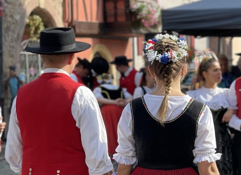 A person in traditional attire with a flower crown and a man in a red vest and black hat. 4