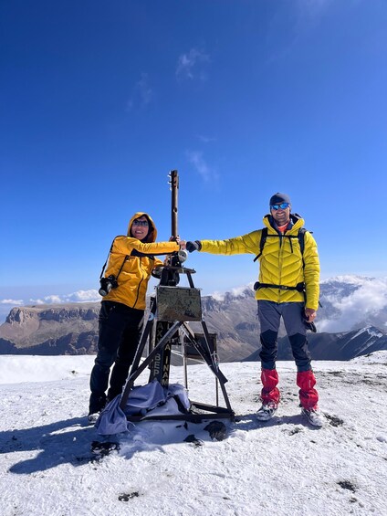 Deux personnes portant des vestes jaunes se trouvent sur une montagne enneigée, sous un ciel dégagé. 1