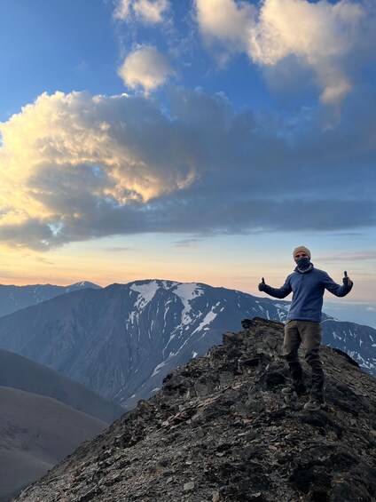 Une personne se tient au sommet d’une montagne rocheuse, avec des montagnes enneigées en arrière-plan. 2