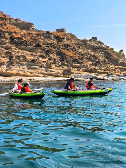 Three people kayaking on a calm body of water with rocky hills in the background. 2
