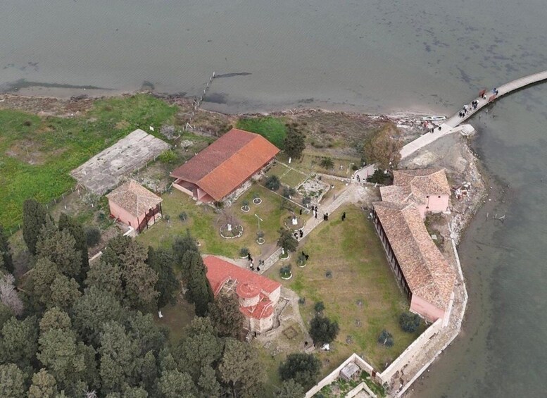 An aerial view of a coastal fort with a red-roofed building, a lighthouse, and a beach with people. 3