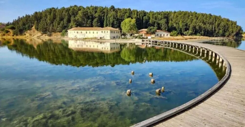 A calm lake with a wooden dock, surrounded by dense forest and a building. 4
