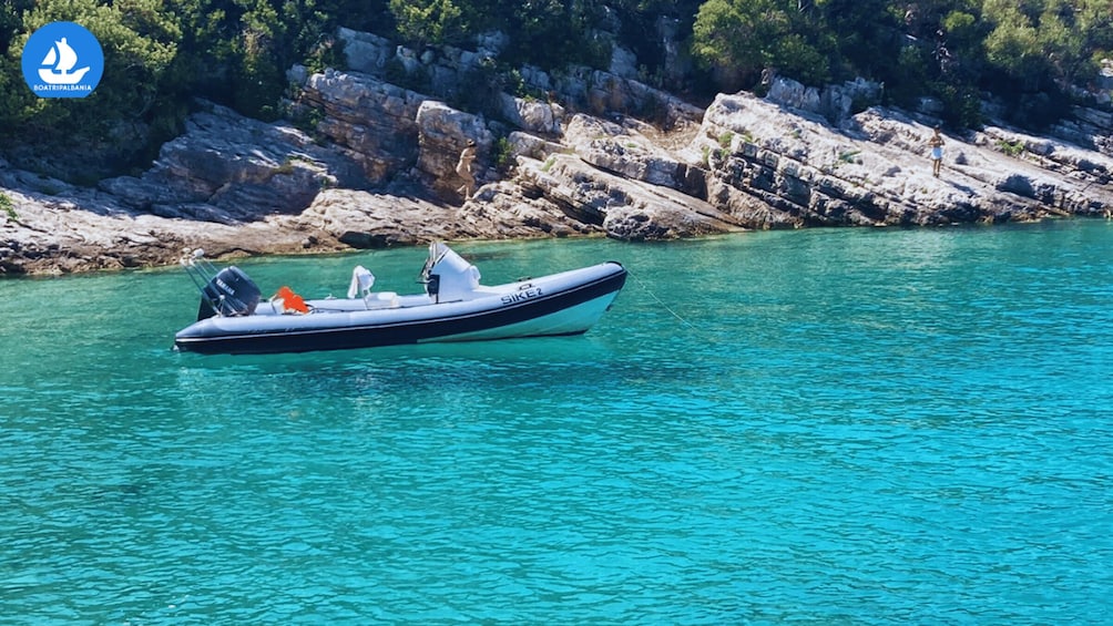 A boat named 'SIKEZ' on clear turquoise water with rocky cliffs in the background. 3