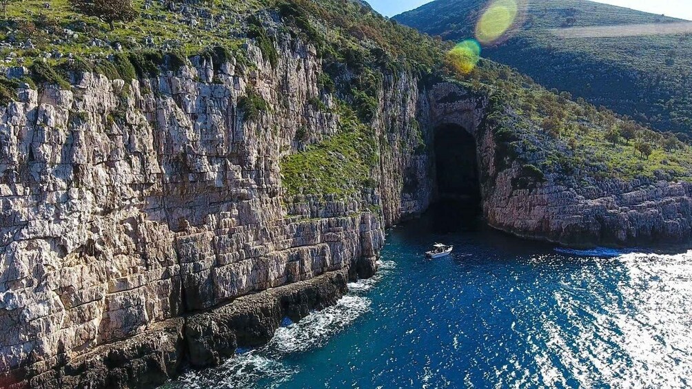 A coastal cliff with a cave entrance and a boat in the water. 5