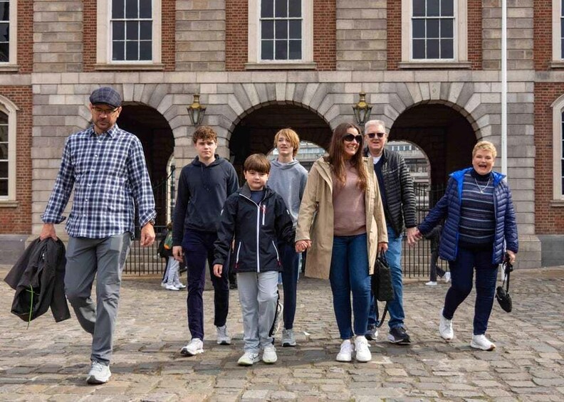 A group of people walking in front of a historic building with arched doorways. 1
