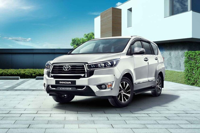 A white Toyota INNOVA CRYSTRA SUV parked in front of a modern house with a clear blue sky. 3