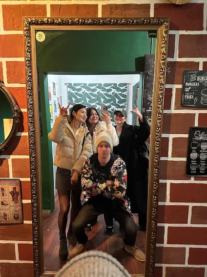 A group of people taking a selfie in front of a mirror with a brick wall and a menu board in the background. 3