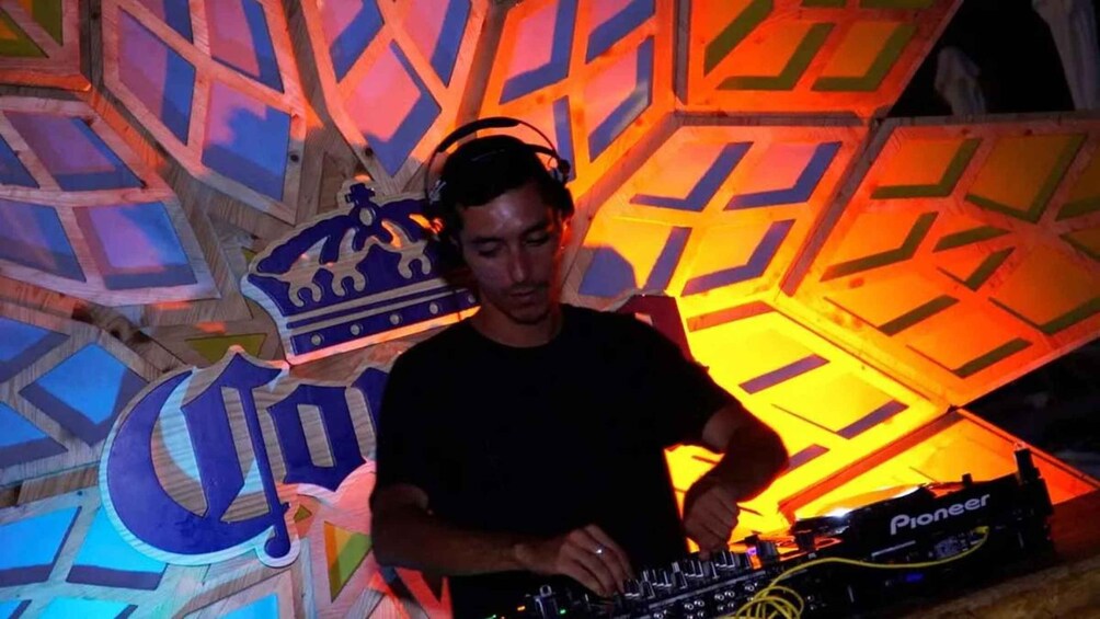 A person DJing with a Pioneer mixer, surrounded by colorful geometric wall decorations. 3