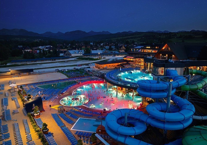 A water park with a large pool, slides, and a seating area at night. 3