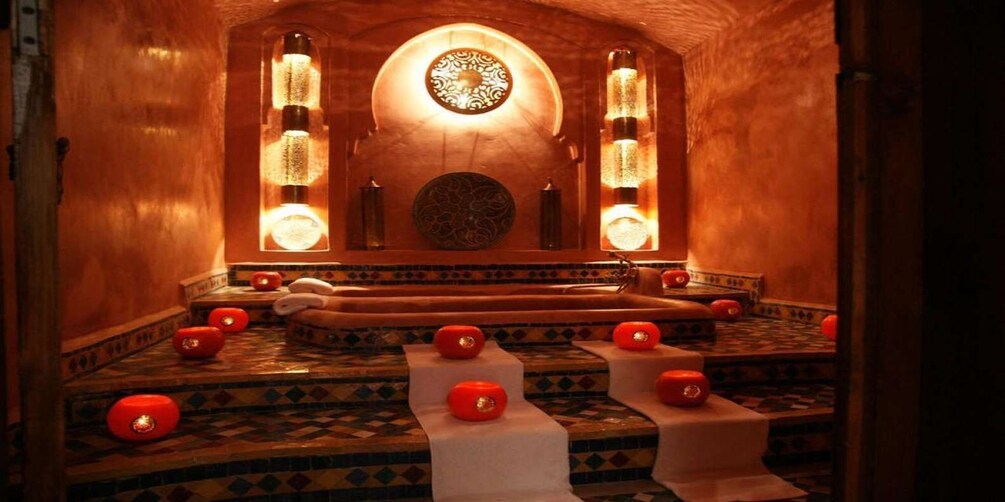 A traditional bath area with a patterned floor, a central seating area, and decorative wall sconces. 5