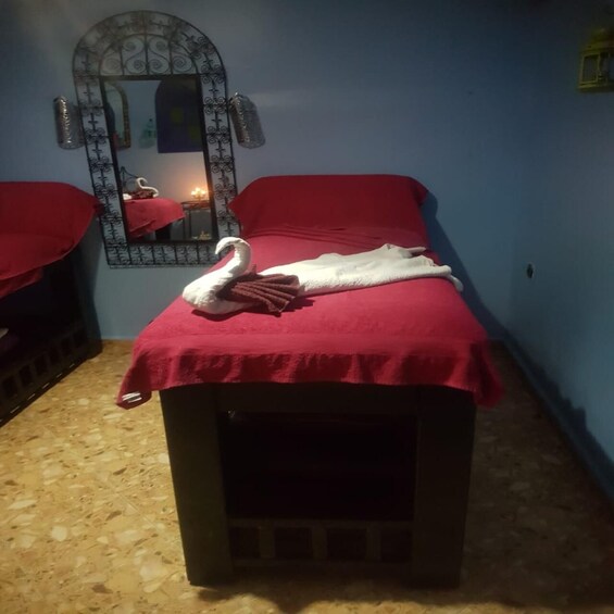 A massage table with a red towel and a white towel, a swan-shaped towel, and a mirror with a decorative frame. 4