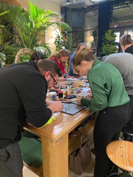 A group of people engaged in a craft activity at a wooden table with various tools and materials. 4