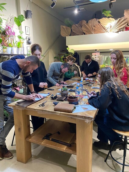 A group of people at a wooden table with a laptop, writing materials, and a potted plant. 3