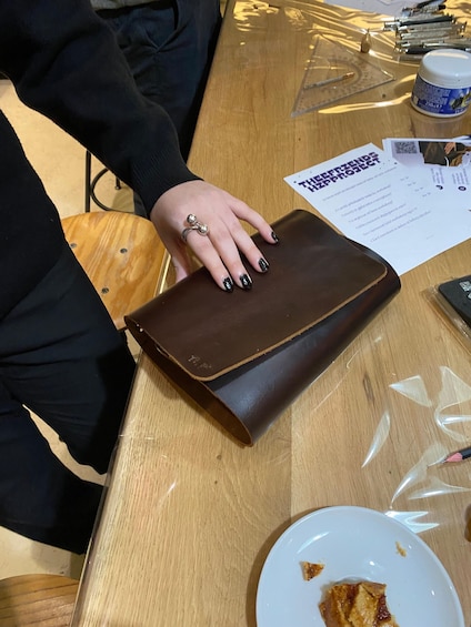 A person holding a brown leather wallet on a wooden table with a plate of food and papers. 5