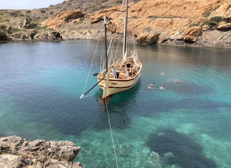 A sailboat anchored in clear turquoise waters with rocky cliffs in the background. 5