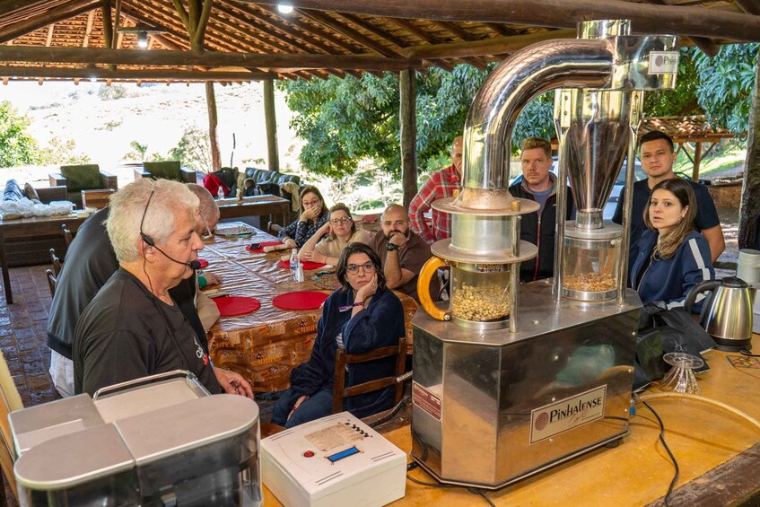 A group of people around a coffee roasting machine outdoors. 3