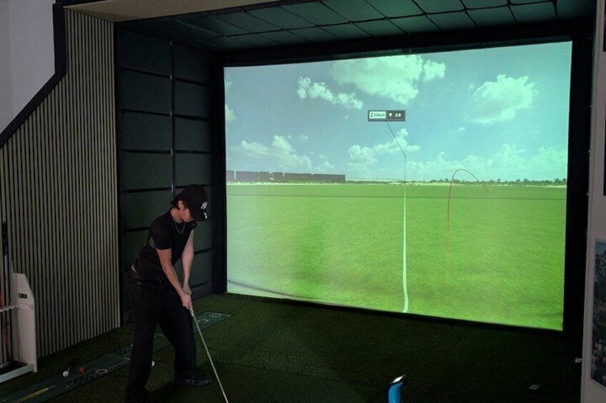A person playing golf indoors with a large screen displaying a golf course. 3