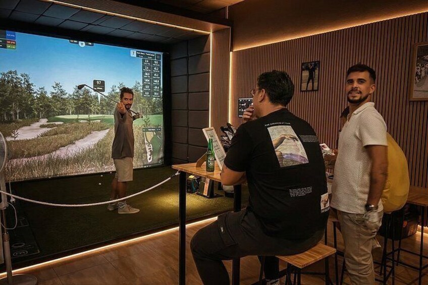 A person playing a golf video game, another person observing, and a third person holding a camera. 5
