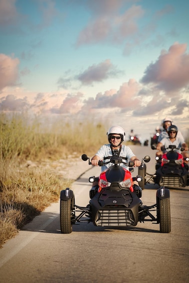 A group of people riding ATVs on a paved path with grass on the sides and a cloudy sky in the background. 4