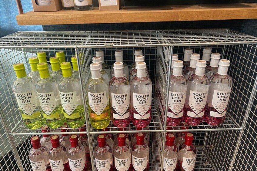 En metallhylla med flaskor av South Loch Gin i olika färger. 5
